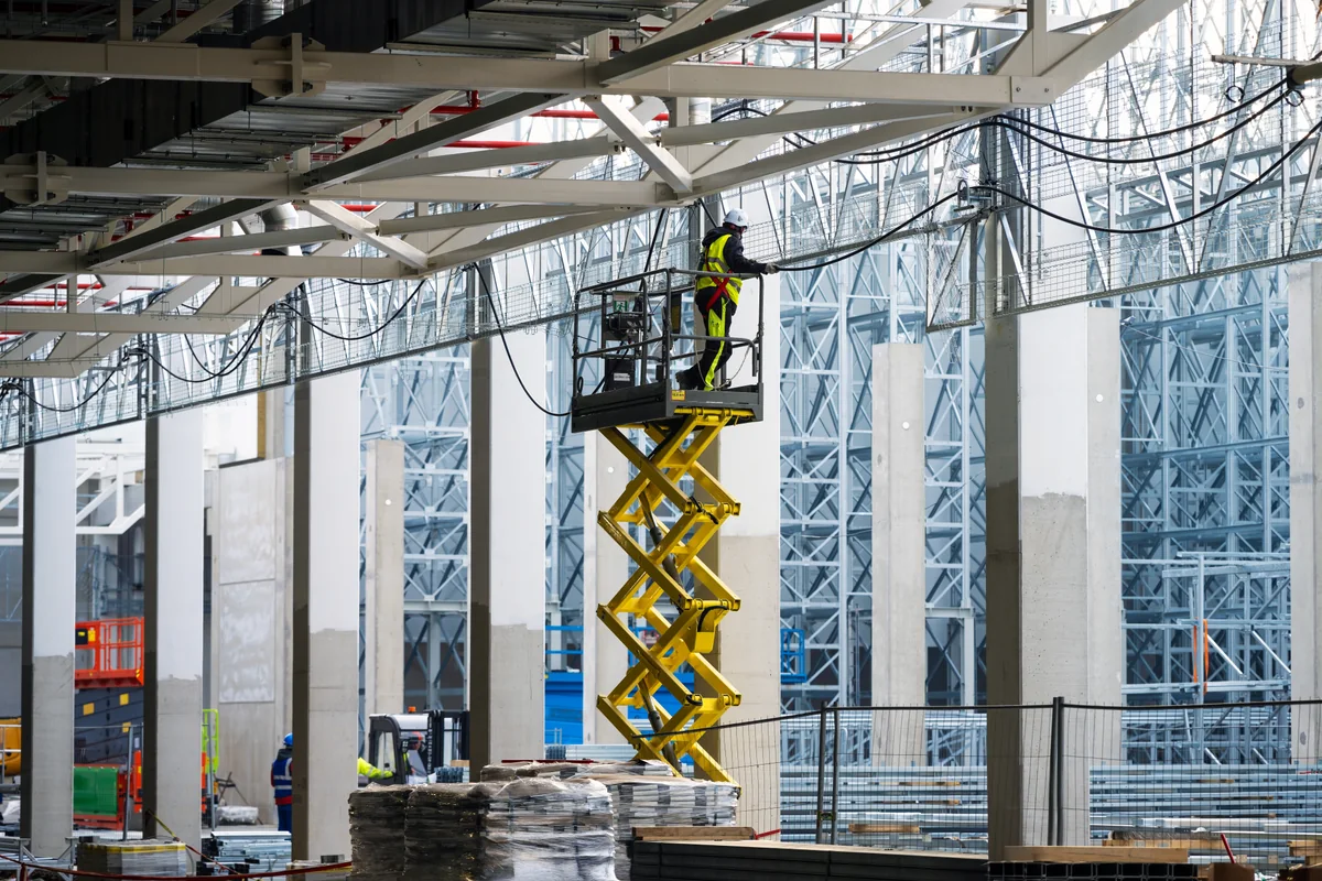 Elektriker installerar kablar från en saxlift i en större byggnad.